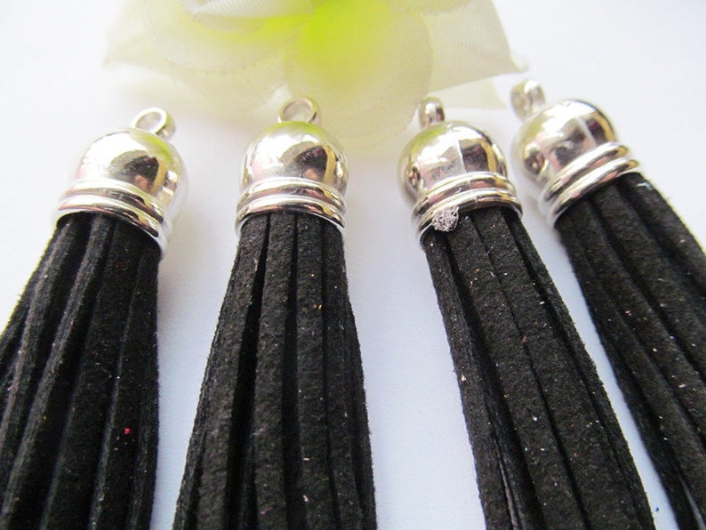 May include: Four black suede tassels with silver metal caps. The tassels are approximately 2 inches long.