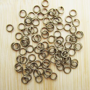 May include: A large pile of small, gold-toned jump rings. The rings are all the same size and are arranged in a random pattern.