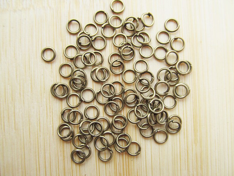 May include: A large pile of small, gold-toned jump rings. The rings are all the same size and are arranged in a random pattern.