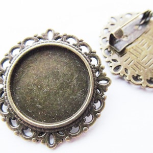 May include: Two antique bronze round metal frames with a decorative filigree design. One frame has a pin back, the other has a blank centre.