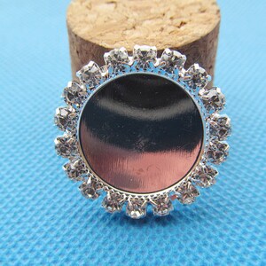 May include: Silver-toned round bezel with a clear glass insert and a border of clear rhinestones.