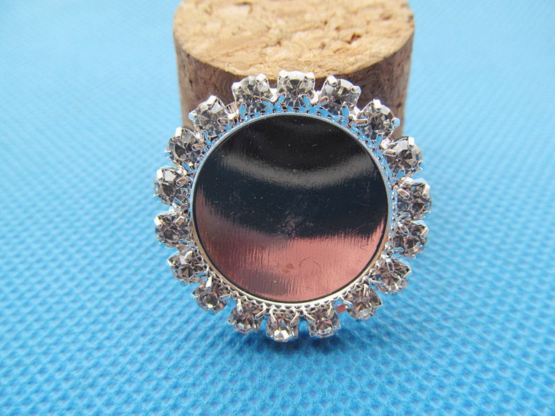 May include: Silver-toned round bezel with a clear glass insert and a border of clear rhinestones.