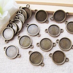 May include: A collection of 18 antique bronze-coloured metal round pendant trays with a smooth, slightly textured surface. Each tray has two loops on the side for attaching a chain or cord.