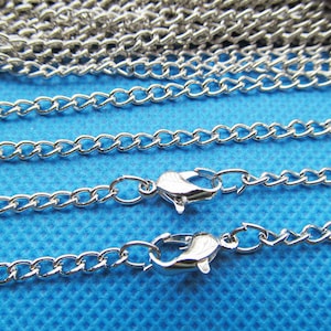 May include: Three silver chains with lobster claw clasps on a blue background. The chains are different lengths and are arranged in a staggered pattern.