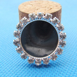 May include: Silver round bezel with clear rhinestones surrounding a black circle.