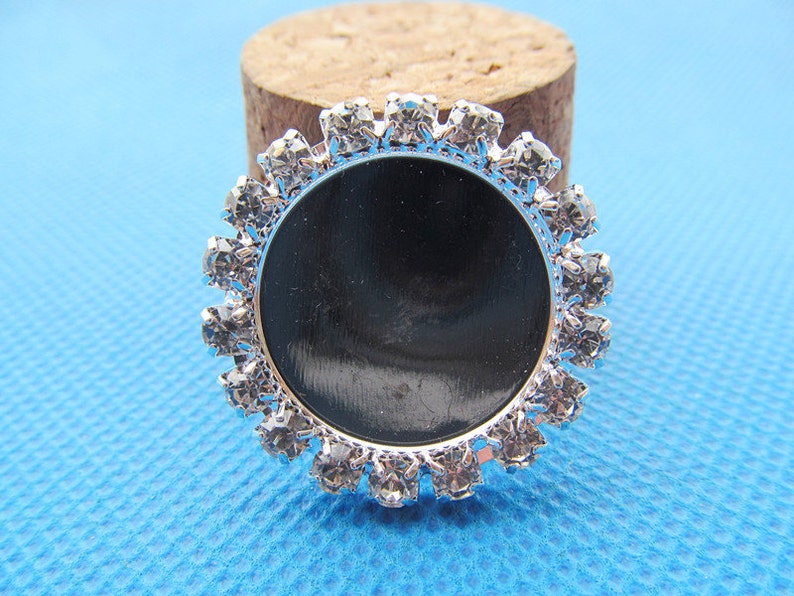 May include: Silver round bezel with clear rhinestones surrounding a black circle.