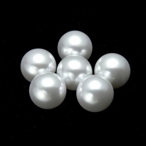 May include: Six white pearl beads arranged in a circular pattern on a black background.
