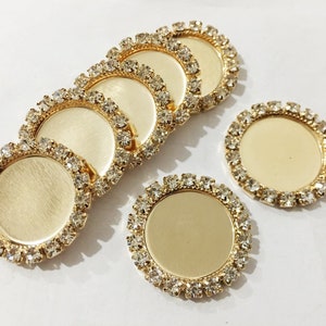 May include: Six gold-toned round metal trays with clear rhinestone borders. The trays are blank and can be used for crafts or jewelry making.