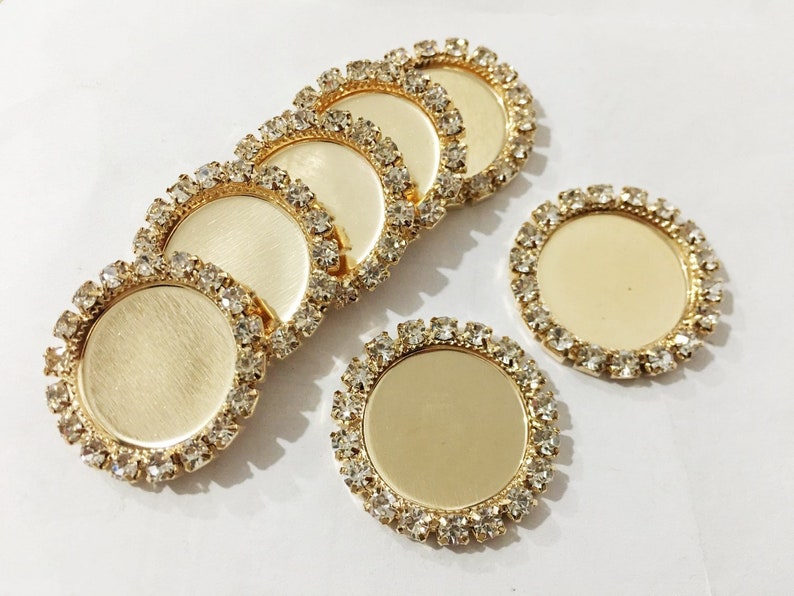 May include: Six gold-toned round metal trays with clear rhinestone borders. The trays are blank and can be used for crafts or jewelry making.