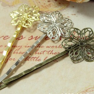 May include: Three gold, silver, and bronze hair clips with decorative flower designs. The flowers are intricate and have a delicate, lacy look.