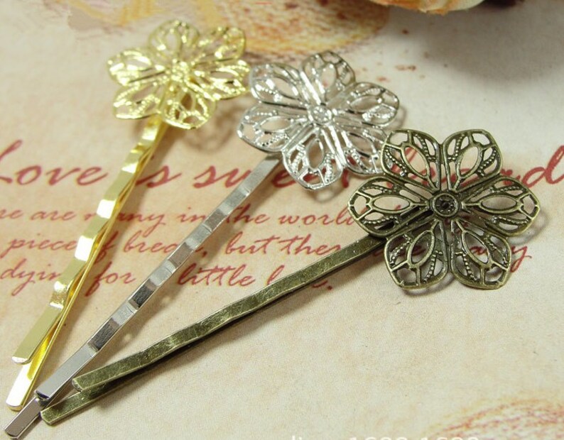 May include: Three gold, silver, and bronze hair clips with decorative flower designs. The flowers are intricate and have a delicate, lacy look.