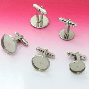 Può includere: Cinque gemelli d'argento con inserti rotondi in vetro trasparente. I gemelli sono progettati per essere personalizzati con immagini o altri abbellimenti.