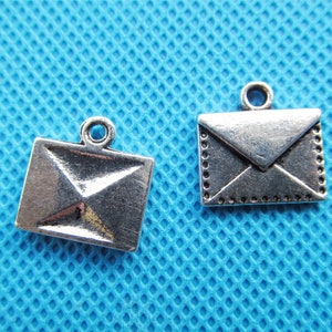May include: Two silver envelope charms with a loop for hanging. The charms are on a blue background.