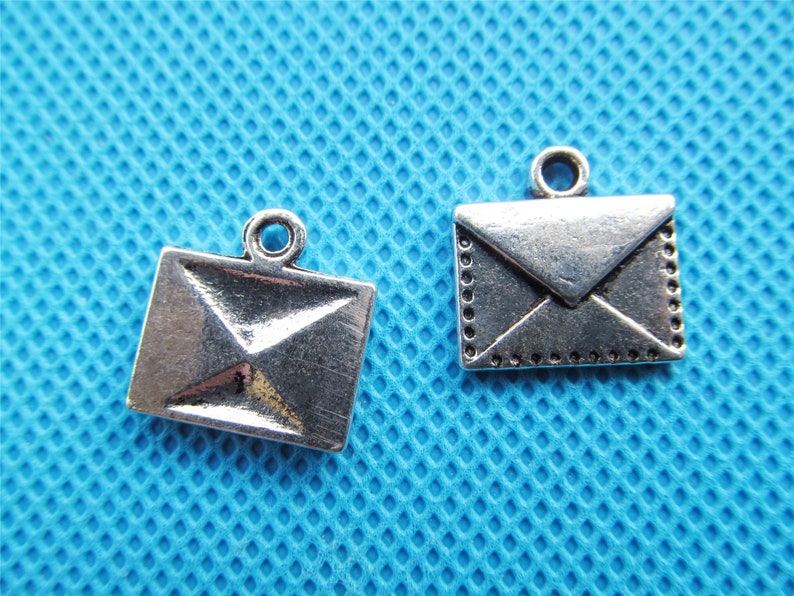 May include: Two silver envelope charms with a loop for hanging. The charms are on a blue background.