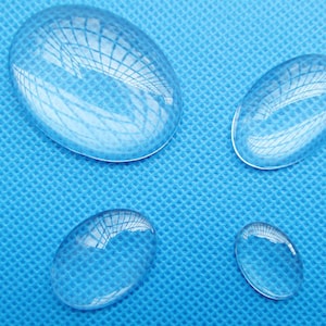Peut inclure: Quatre lentilles grossissantes ovales en verre transparent de différentes tailles sur une surface texturée bleue.