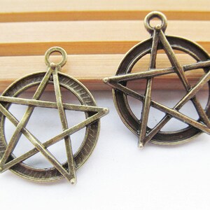 May include: Two antique bronze metal charms in the shape of a five-pointed star with a circle around it.