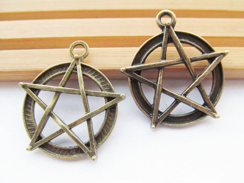 May include: Two antique bronze metal charms in the shape of a five-pointed star with a circle around it.
