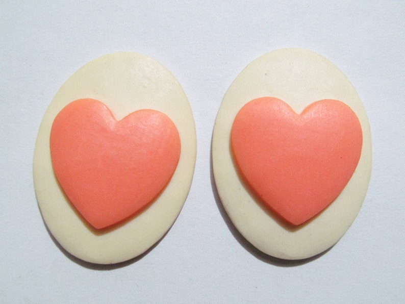 May include: A pair of white oval-shaped earrings with a pink heart design.