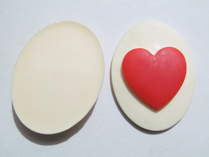 May include: A white oval-shaped trinket box with a red heart-shaped design on the lid. The box is open, revealing an empty interior.