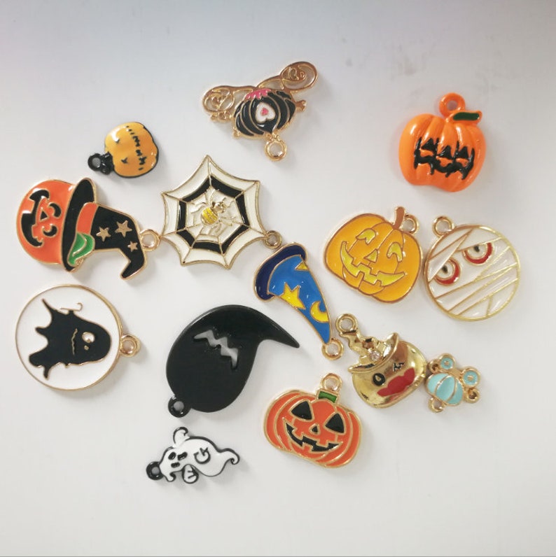 May include: Assortment of Halloween-themed charms, including pumpkins, ghosts, bats, witches hats, and a spider web. The charms are made of metal and have a gold finish.