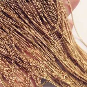 May include: A close-up of a bundle of gold-colored chain links. The chain is made of a thin, delicate metal and has a slightly textured surface.