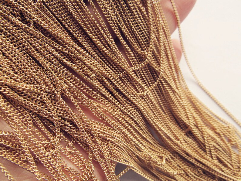 May include: A close-up of a bundle of gold-colored chain links. The chain is made of a thin, delicate metal and has a slightly textured surface.