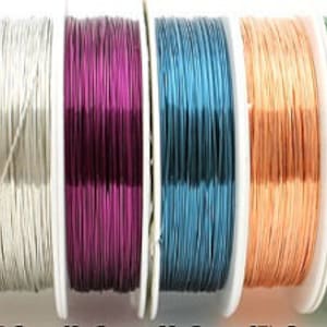 Op de afbeelding: Spoelen met gekleurde draad in verschillende kleuren, waaronder zwart, rood, zilver, paars, blauw, perzik, groen en goud. De draad is gewikkeld rond spoelen met wit plastic.