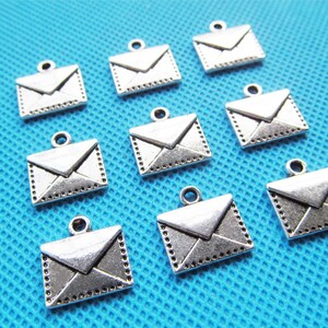 May include: Ten silver-toned metal envelope charms with a detailed design. The charms are perfect for adding a touch of vintage style to jewelry or crafts.