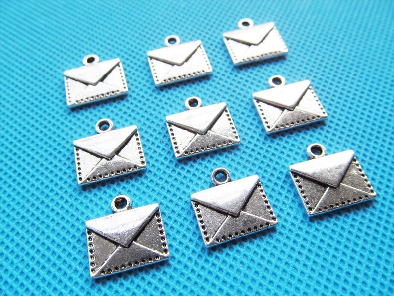 May include: Ten silver-toned metal envelope charms with a detailed design. The charms are perfect for adding a touch of vintage style to jewelry or crafts.