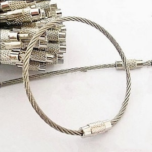 May include: A collection of silver key rings made of braided steel wire. The key rings are circular with a screw-on closure. The background is white.