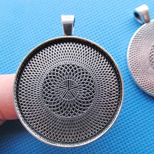 May include: Silver-toned pendant with a circular, patterned design. The pendant has a loop at the top for attaching a chain.