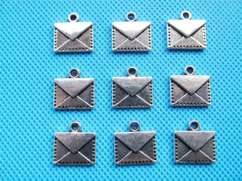 May include: Ten silver-toned metal envelope charms with a loop at the top for attaching to jewelry or crafts. The charms are about 1 inch in size and have a detailed design.