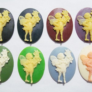 May include: Eight oval-shaped resin cabochons with a raised design of a fairy holding flowers. The cabochons are in various colors, including black, green, purple, red, blue, and white.