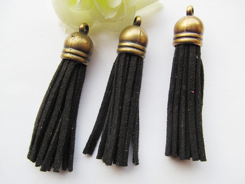 May include: Three black suede tassels with gold metal tops. The tassels are approximately 2 inches long.
