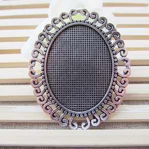 May include: Silver oval-shaped pendant with a decorative filigree border. The pendant has a mesh-like surface in the center.