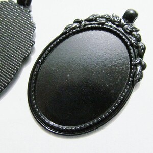 Puede incluir: Dos bandejas ovaladas de metal negro para colgantes con un borde decorativo. Una bandeja tiene una superficie lisa y la otra una superficie texturizada.