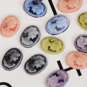 May include: Assortment of oval-shaped cameo-style buttons in various colors, including pink, blue, gray, green, and purple. The buttons feature a raised design of a woman's profile.