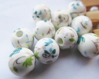 May include: A collection of white ceramic beads with a floral design in shades of green and blue. The beads have a hole in the center for stringing.