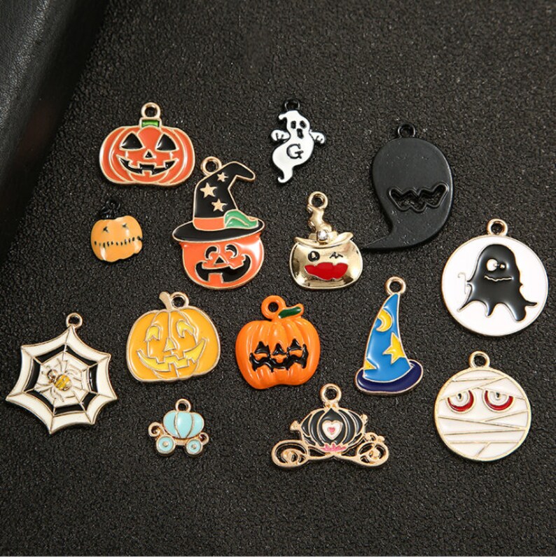 May include: Assortment of Halloween themed metal charms, including pumpkins, ghosts, witches hats, spiders, and a carriage. The charms are gold-toned and have colorful enamel details.