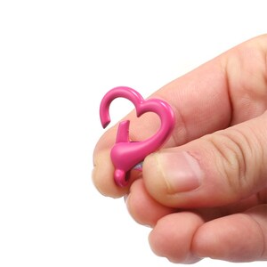 May include: Pink heart-shaped metal clasp for attaching items to a keychain, bag, or other accessories.