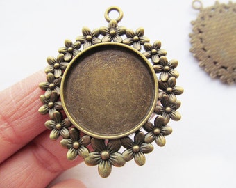 May include: A round antique bronze pendant tray featuring a circular center bezel surrounded by a decorative border of small five-petaled flowers. The pendant includes a small loop at the top for attachment, with a matching piece visible in the background.