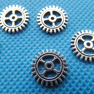 May include: Six silver metal gears of varying sizes on a blue textured background.