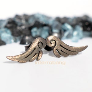 May include: A pair of silver angel wing earrings with a detailed design. The wings are slightly curved and have a textured surface.