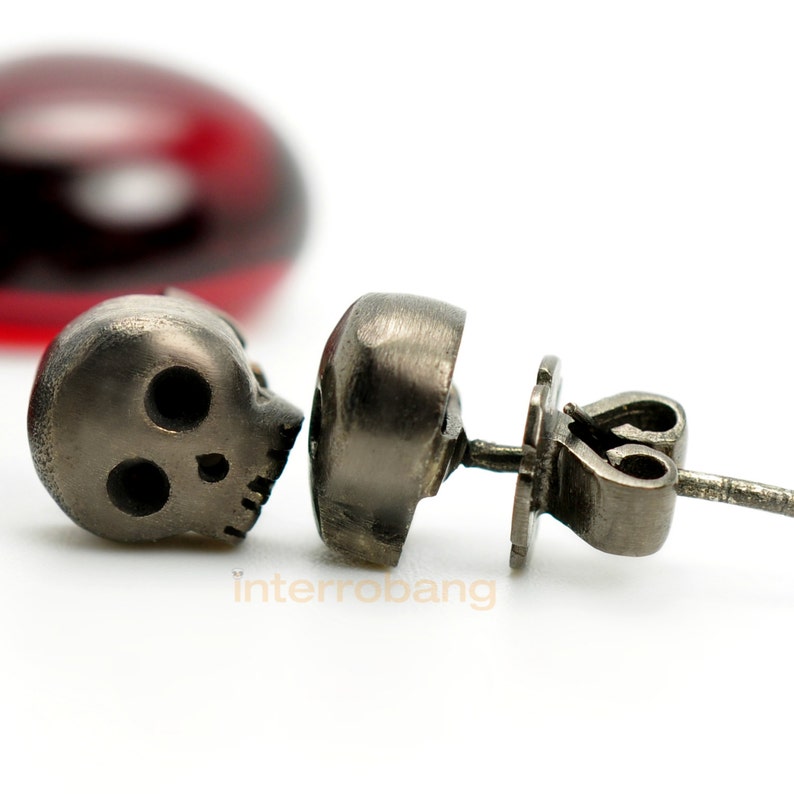 May include: A pair of silver skull stud earrings. The earrings are made of metal and feature a skull design. The skull is detailed with eye sockets and a nose.
