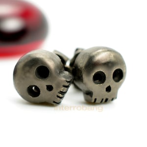 May include: A pair of silver skull earrings. The skulls are detailed with eye sockets, a nose, and a mouth.