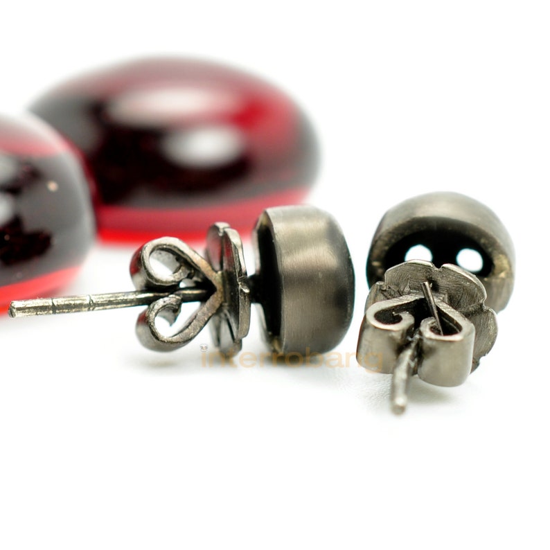 May include: A pair of silver stud earrings with a decorative design. The earrings have a dark grey finish and a small, round stone in the centre.