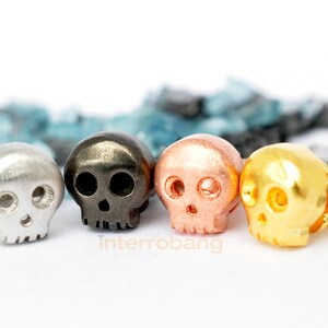 May include: Four small skull-shaped earrings in silver, black, copper, and gold.