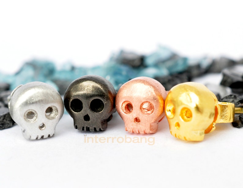 May include: Four small skull-shaped earrings in silver, black, copper, and gold.