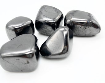 May include: Five smooth, dark gray hematite tumbled stones. The stones are various shapes and sizes, with a slightly metallic sheen.