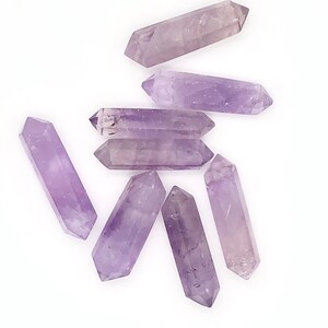 May include: A group of seven amethyst crystal points, each with a double-pointed shape, arranged on a white background. The crystals are a light purple color and have a smooth, polished finish.